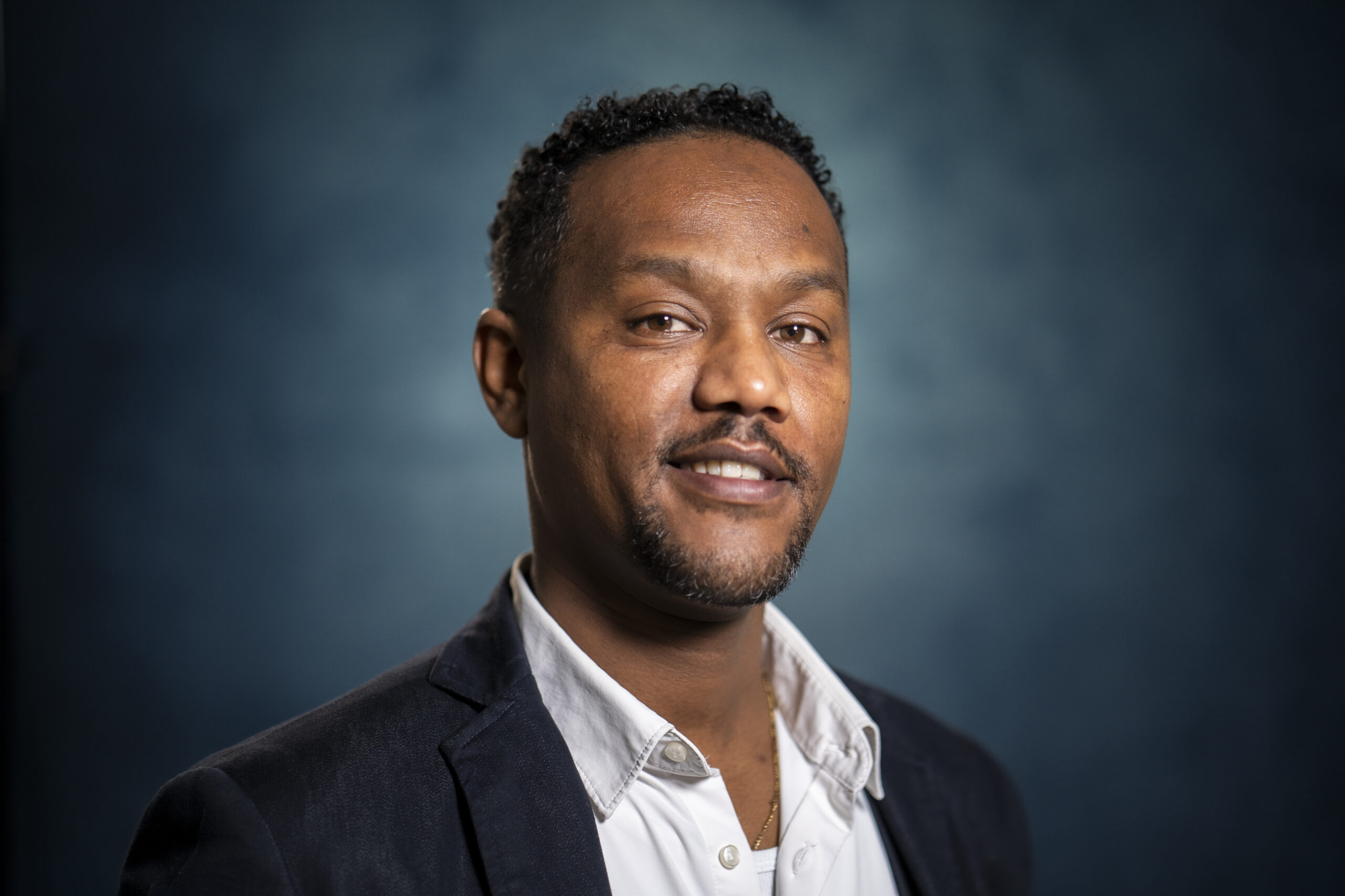 Eritrea – Robel A guy with a middle dark skin, white blouse and jacket, looks into the camera.