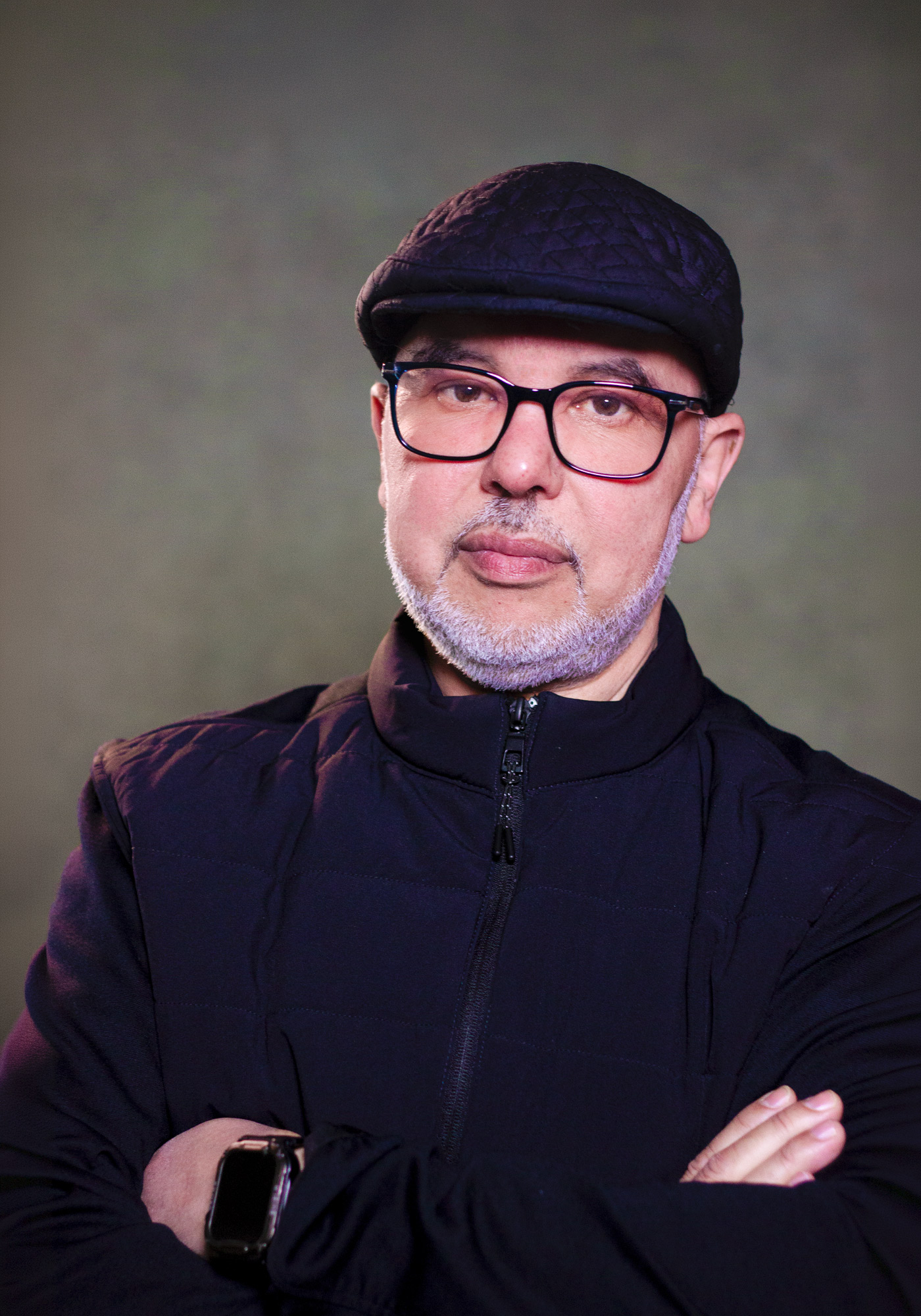 Je ziet een man met een petje en bril die in de camera kijkt